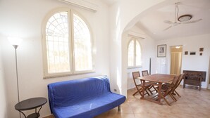 Een kamer met een blauwe bank, een eettafel met stoelen en een plafondventilator.