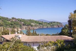 A coastal property with a tiled roof, surrounded by greenery and overlooking a bay with a mountain in the background. - RESIDENZA IL GABBIANO - VILLINO LE SUGHERE (Capoliveri)