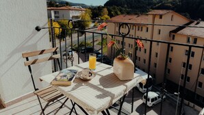 A balcony with a table set for two, a book, a cup, and a vase with flowers.