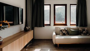 A modern living room with a wooden cabinet, a sofa with patterned cushions, and a large flat-screen TV mounted on the wall.