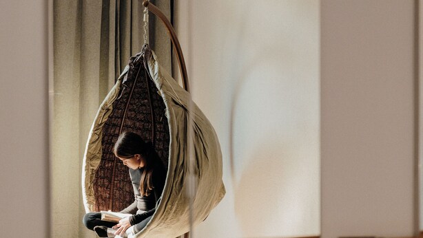 A room with a hanging chair, a wooden floor, and a large mirror reflecting the room.