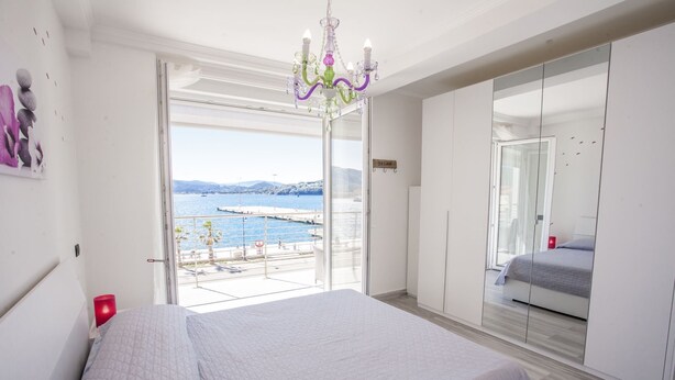 A bedroom with a bed, a large mirror, and a view of the sea.