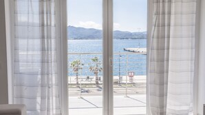 A room with a large window overlooking a coastal area with a dock and palm trees.