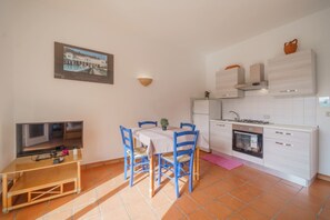 A compact kitchen with white cabinets, a built-in oven, and a small dining area with blue chairs and a table. - APP.TI BAIA BLU - BAIA BLU 3 (Portoferraio)