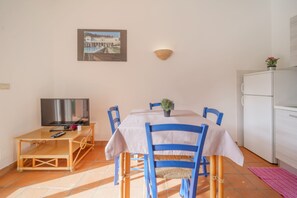 A dining area with a table and chairs, a television, and a refrigerator. - APP.TI BAIA BLU - BAIA BLU 3 (Portoferraio)