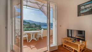 A balcony with a table and chairs, a TV, and a scenic view of a coastal area. - APP.TI BAIA BLU - BAIA BLU 3 (Portoferraio)