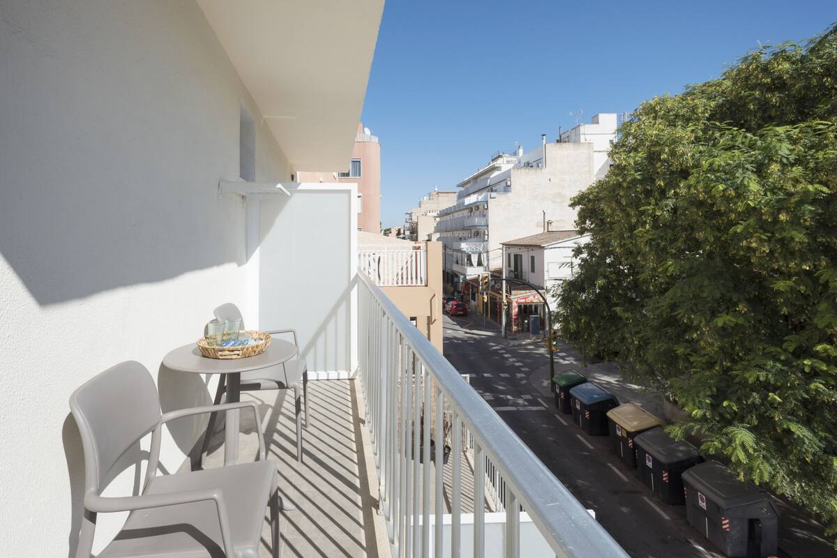 Ein Balkon mit Tisch und Stühlen, mit Blick auf eine Straße mit parkenden Autos und Gebäuden.