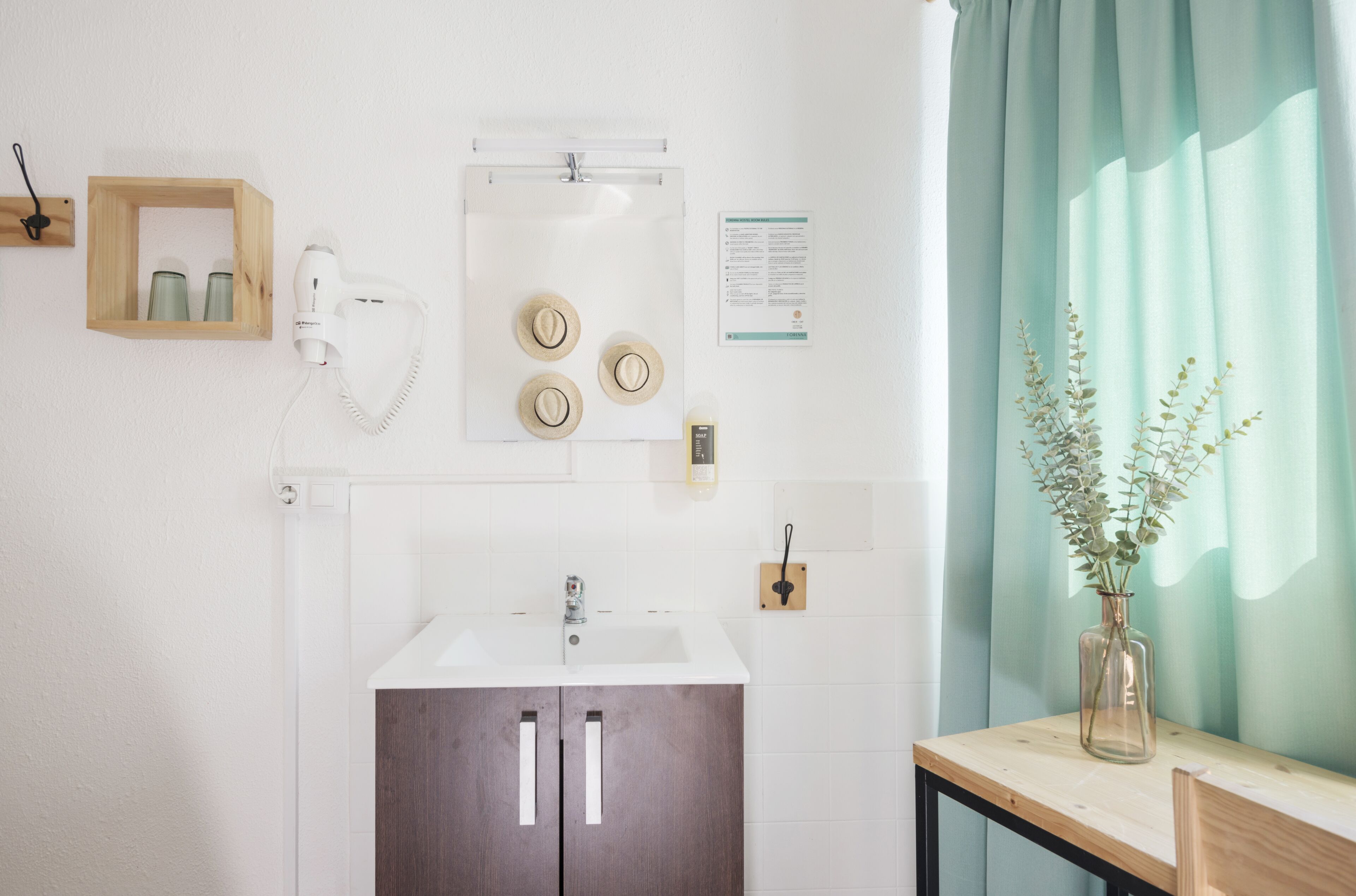 Un baño con lavamanos, espejo y secador de pelo en la pared.