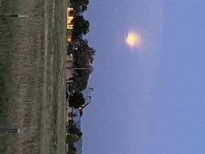 Ein nächtliches Landschaftsbild mit Vollmond, einer grünen Wiese und einem Gebäude mit beleuchteten Fenstern.