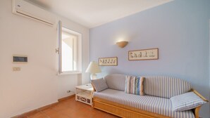 A room with a striped sofa, a small table with a lamp, a window, and two wall-mounted pictures. - APP.TI BAIA BLU - BAIA BLU 5 (Portoferraio)