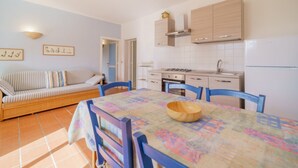 A compact kitchen with a dining area, featuring a sofa, chairs, and a table with a patterned tablecloth. - APP.TI BAIA BLU - BAIA BLU 5 (Portoferraio)