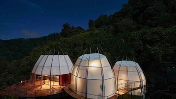 Three dome-shaped structures with wooden decks and stairs, surrounded by lush greenery and a starry night sky.