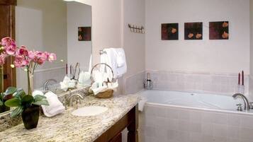 Une salle de bain avec un comptoir en granit, un lavabo, une grande baignoire et un miroir. On y trouve des serviettes et un panier sur le comptoir.