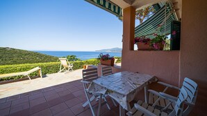 Una terrazza con tavolo e sedie, vista sul mare e un balcone con piante in vaso.