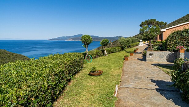 Un sentiero in pietra che conduce a un edificio con vista sul mare e sulle colline.