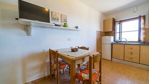 Una piccola cucina con mobili in legno, un frigorifero bianco, una finestra con tende e un tavolo con sedie.