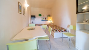 A small, brightly lit room with a single table and two chairs, a bed with colorful bedding, a TV on a shelf, and a lamp on a bedside table. - APP.TI CASA SERENA - CASA SERENA BILO 3 (Capoliveri)