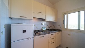 A compact kitchen with white cabinets, a built-in refrigerator, a gas stove, and a window providing natural light. - APP.TI CASA SERENA - CASA SERENA BILO 3 (Capoliveri)