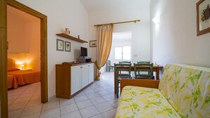 A cozy living room with a sofa, a TV, a dining table with chairs, and a kitchen area with cabinets. - APP.TI CASA SERENA - CASA SERENA TRILO 4 (Capoliveri)
