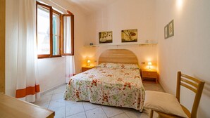 A bedroom with a bed, two bedside tables, a chair, a window with curtains, and wall-mounted lights. - APP.TI CASA SERENA - CASA SERENA TRILO 4 (Capoliveri)