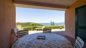 A balcony with a table and chairs, overlooking a scenic view of the sea and hills. - APP.TI CASA SERENA - CASA SERENA TRILO 4 (Capoliveri)