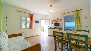 Une pièce comprenant un lit, une table à manger avec des chaises, un téléviseur et un coin cuisine visible à travers une porte ouverte.