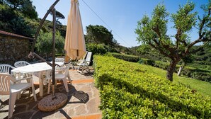 Une terrasse extérieure avec un sol en pierre, des chaises en plastique blanches, une table et un grand parasol.