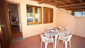 Un coin repas avec une table dressée pour deux personnes, entouré de chaises en plastique blanches, sous un plafond en bois.