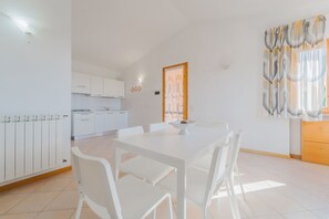 Een moderne keuken met witte kastjes en een eethoek met een witte tafel en stoelen.