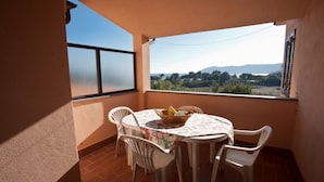 A balcony with a table and chairs, a view of the countryside, and a window with shutters.