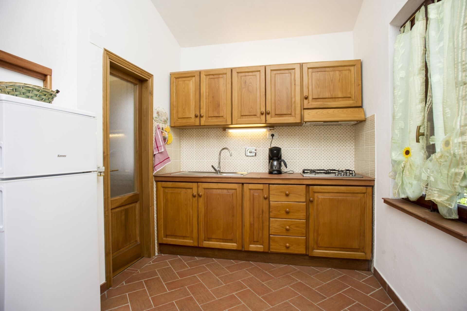 Eine kleine Küche mit Holzschränken, einem weißen Kühlschrank, einem Gasherd und einer gefliesten Spritzschutzwand.