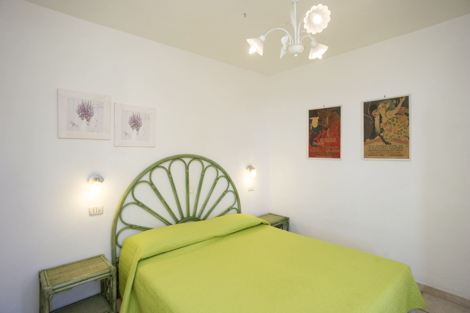 Une chambre avec un lit vert, une tête de lit en métal verte, deux appliques murales et deux tableaux encadrés accrochés au mur.