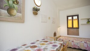 Una camera accogliente e piccola con due letti singoli, una finestra con tende e uno specchio fissato alla parete.