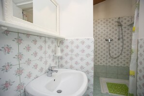 A bathroom with a white sink, a mirror, and a shower area with floral tiles.