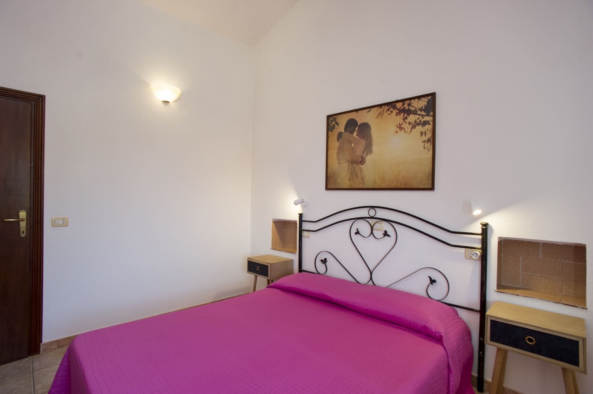 Une chambre à coucher comprenant un lit, une table de chevet, une étagère fixée au mur et un tableau.