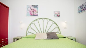 A bed with a green headboard, a green bedspread, and two pillows. There are two wall-mounted light fixtures and two framed floral paintings above the bed. - APP.TI MORCONE - MORCONE BILO 4 (Capoliveri)