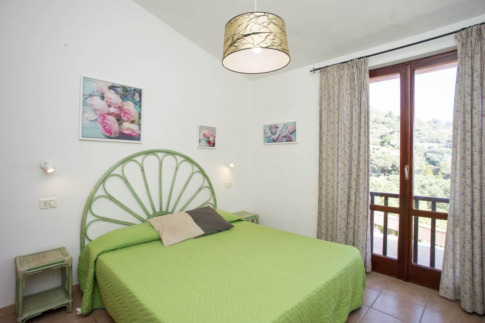 A bedroom with a green bed, a green headboard, and a view of a balcony with curtains.