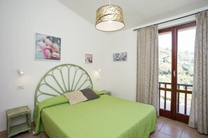 Quarto com cama e cabeceira verdes, e vista para uma varanda com cortinas.