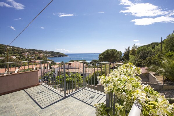 Uma varanda com vista para o mar, um jardim com flores brancas e um chão de azulejos.