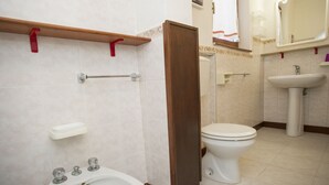 Et badeværelse med toilet, bidet, håndvask og et spejl med lys.