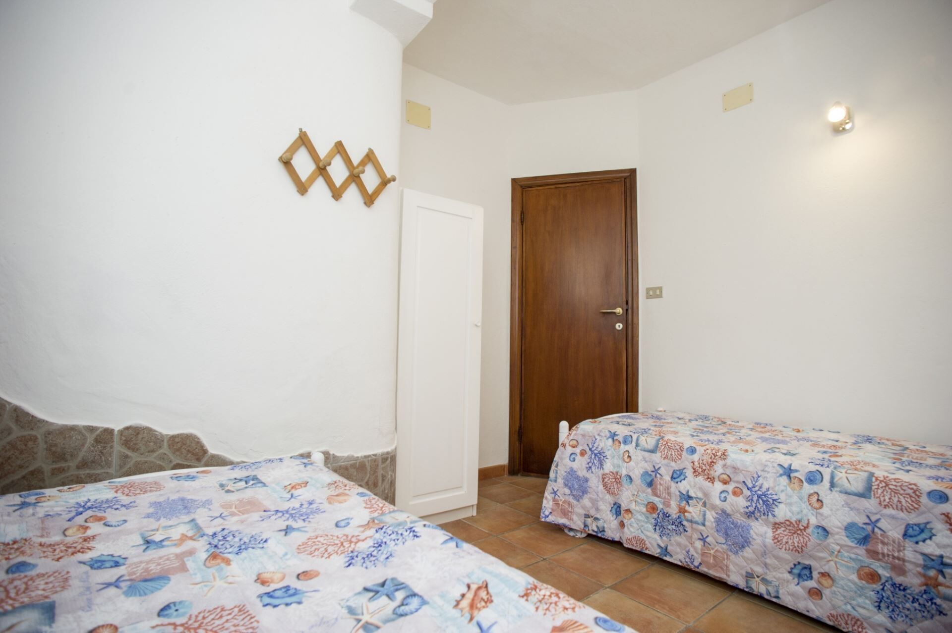A bedroom with two beds, a wooden door, and a wall-mounted light fixture.