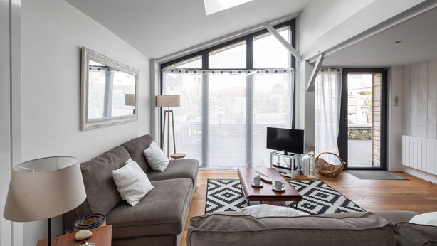 A modern living room with a sofa, coffee table, and TV. Large windows offer a view of the outdoors. - Villa Emeraude, Sublime maison à St Briac (Saint-Briac-sur-Mer)