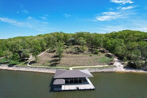 A floating structure with a covered deck, surrounded by a forested hillside and a body of water.