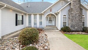 A two-story house with a stone chimney, a front porch, and a driveway leading to the entrance. - A 5500 sq ft.Luxury Home~Huge Boat Dock~Perfect for Large Groups~Waterfront~Pool Table~Firepit (Camdenton)