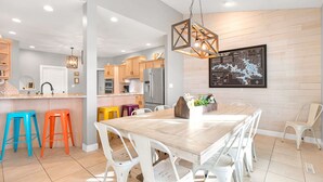 A modern kitchen with wooden cabinets, a stainless steel refrigerator, and a dining area with a wooden table and white chairs. - A 5500 sq ft.Luxury Home~Huge Boat Dock~Perfect for Large Groups~Waterfront~Pool Table~Firepit (Camdenton)