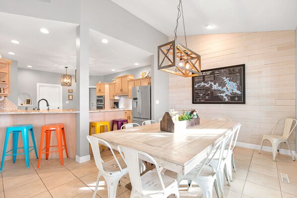 A modern kitchen with wooden cabinets, a stainless steel refrigerator, and a dining area with a wooden table and white chairs. - A 5500 sq ft.Luxury Home~Huge Boat Dock~Perfect for Large Groups~Waterfront~Pool Table~Firepit (Camdenton)