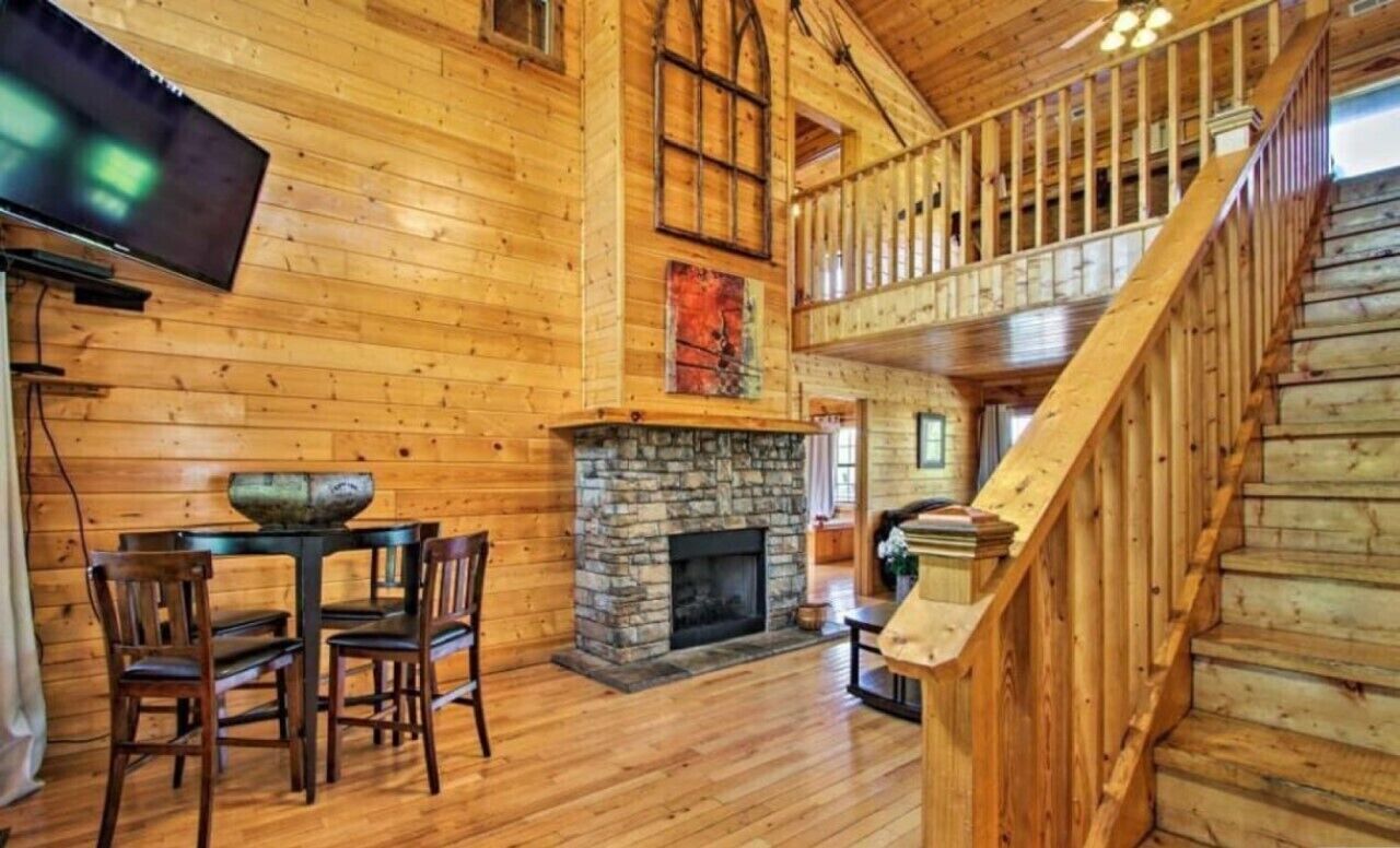 A wooden interior with a fireplace, a dining area with chairs, and a staircase.