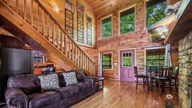 A wooden cabin interior with a leather sofa, dining table, chairs, and a staircase. - Mountain View from front Porch and private Hot tub on the back porch! (Sevierville)
