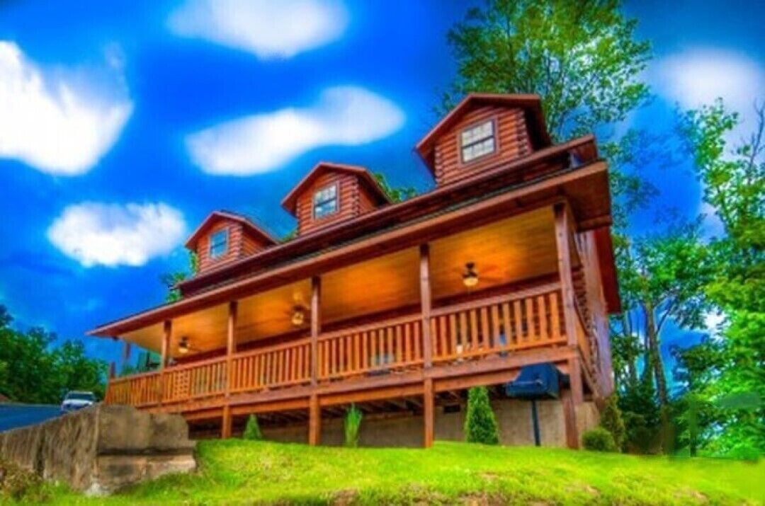A wooden cabin with a porch and multiple windows, surrounded by greenery.