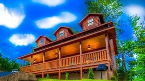 A wooden cabin with a porch and multiple windows, surrounded by greenery. - Mountain View from front Porch and private Hot tub on the back porch! (Sevierville)
